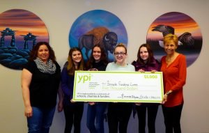 Four female students present a $5000 ceremonial cheque to two charity staff.