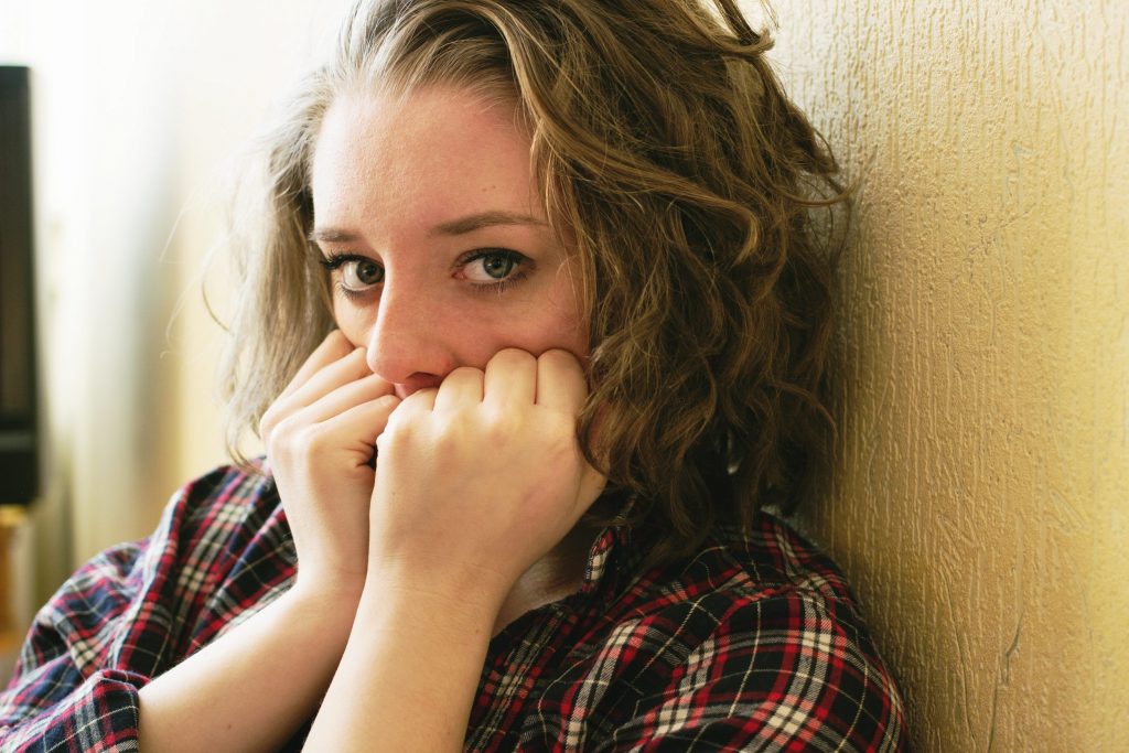A young, frightened woman with her hands up covering part of her face.