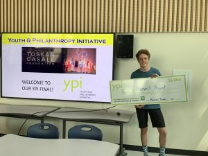 One student holding giant YPI cheque standing in front of PPT presentation screen