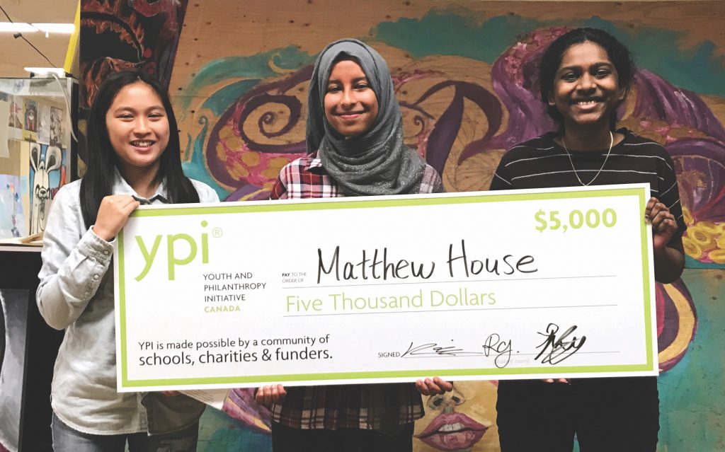Three young women hold up an oversized cheque for $5000 made out to the charity they represented.