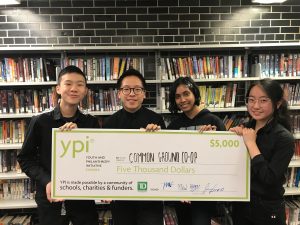 A group of four students holds a cheque for the Common Ground Co-op