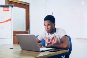 Young black man in a gray t-shirt working on a laptop.